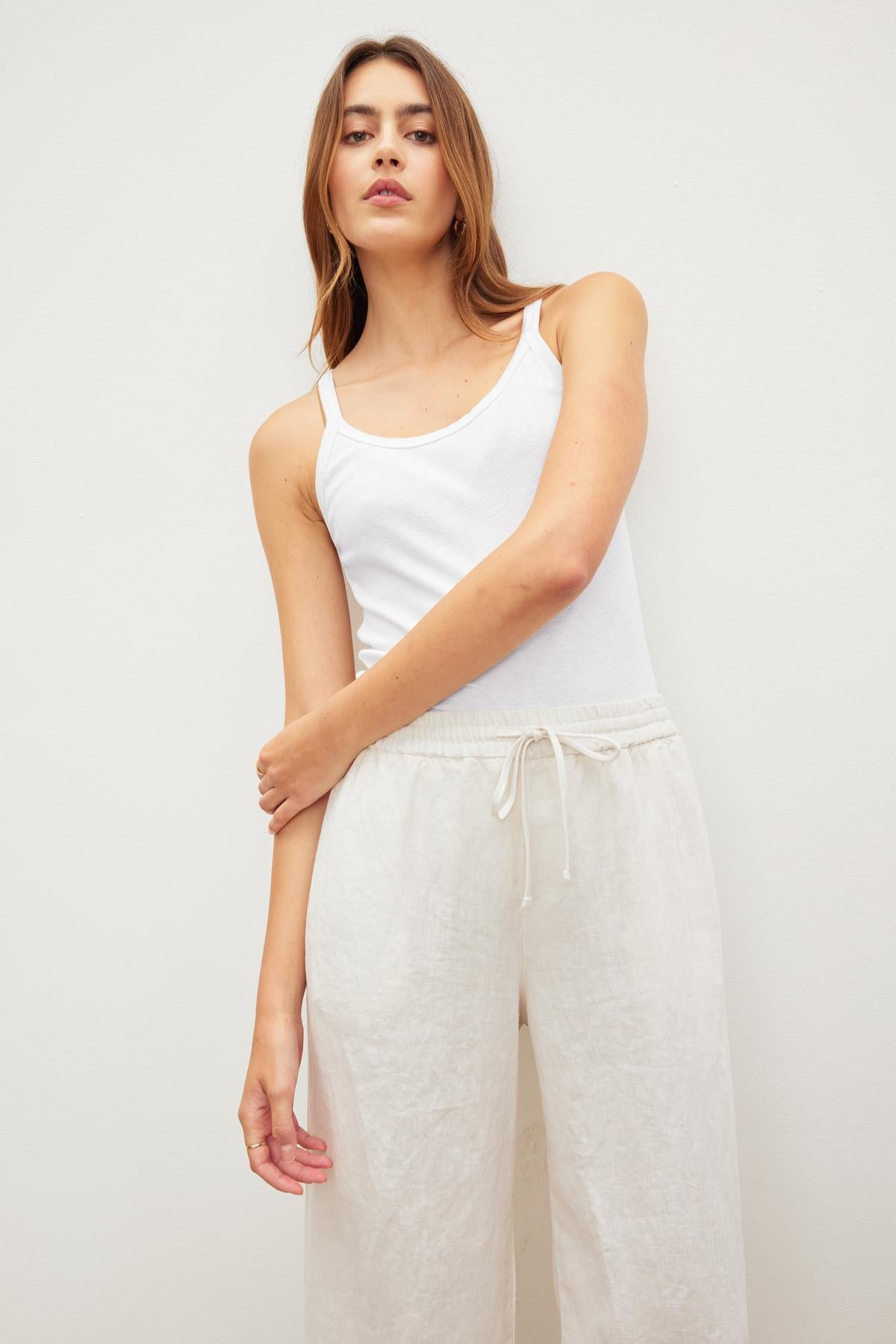 Woman in a white ALIZA RIBBED COTTON LAYERING TANK tank top and linen pants posing against a neutral background. (Velvet by Graham & Spencer)-36443835072705