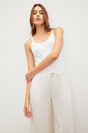 Woman in a white ALIZA RIBBED COTTON LAYERING TANK tank top and linen pants posing against a neutral background. (Velvet by Graham & Spencer)