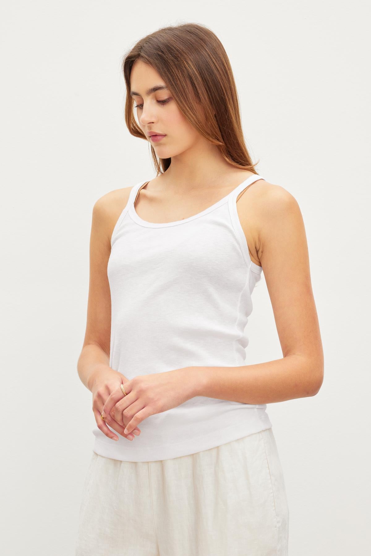 A woman in a white Velvet by Graham & Spencer Aliza Ribbed Cotton Layering Tank with her hands gently clasped in front of her.-36443835105473