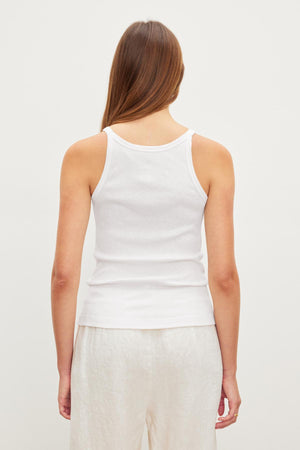 Woman standing with her back to the camera, wearing a white Aliza ribbed cotton layering tank by Velvet by Graham & Spencer and light trousers against a plain background.