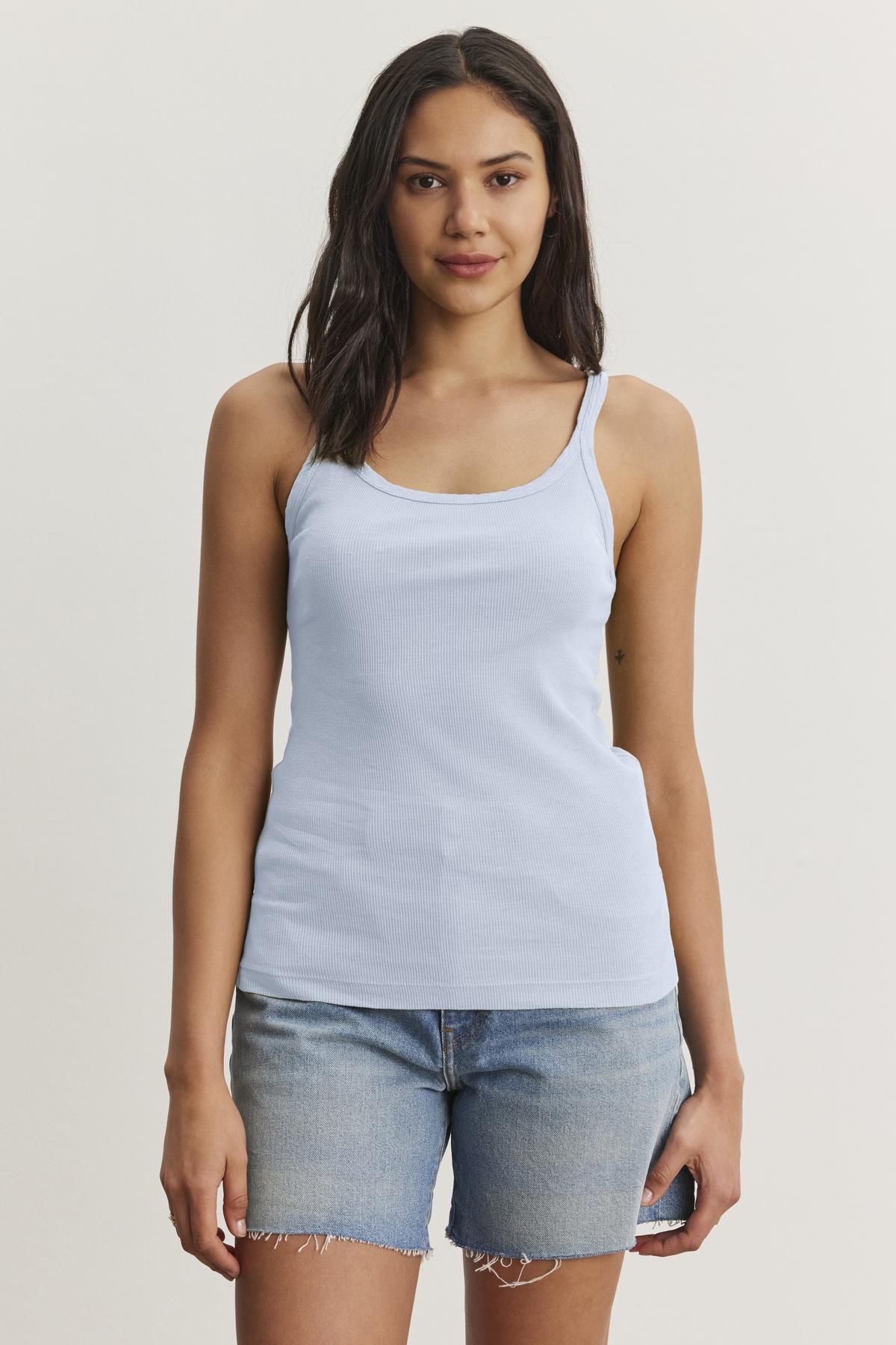 A woman with long dark hair is wearing a light blue ALIZA RIBBED COTTON LAYERING TANK from Velvet by Graham & Spencer and denim shorts. She is standing against a plain white background.-37104335814849