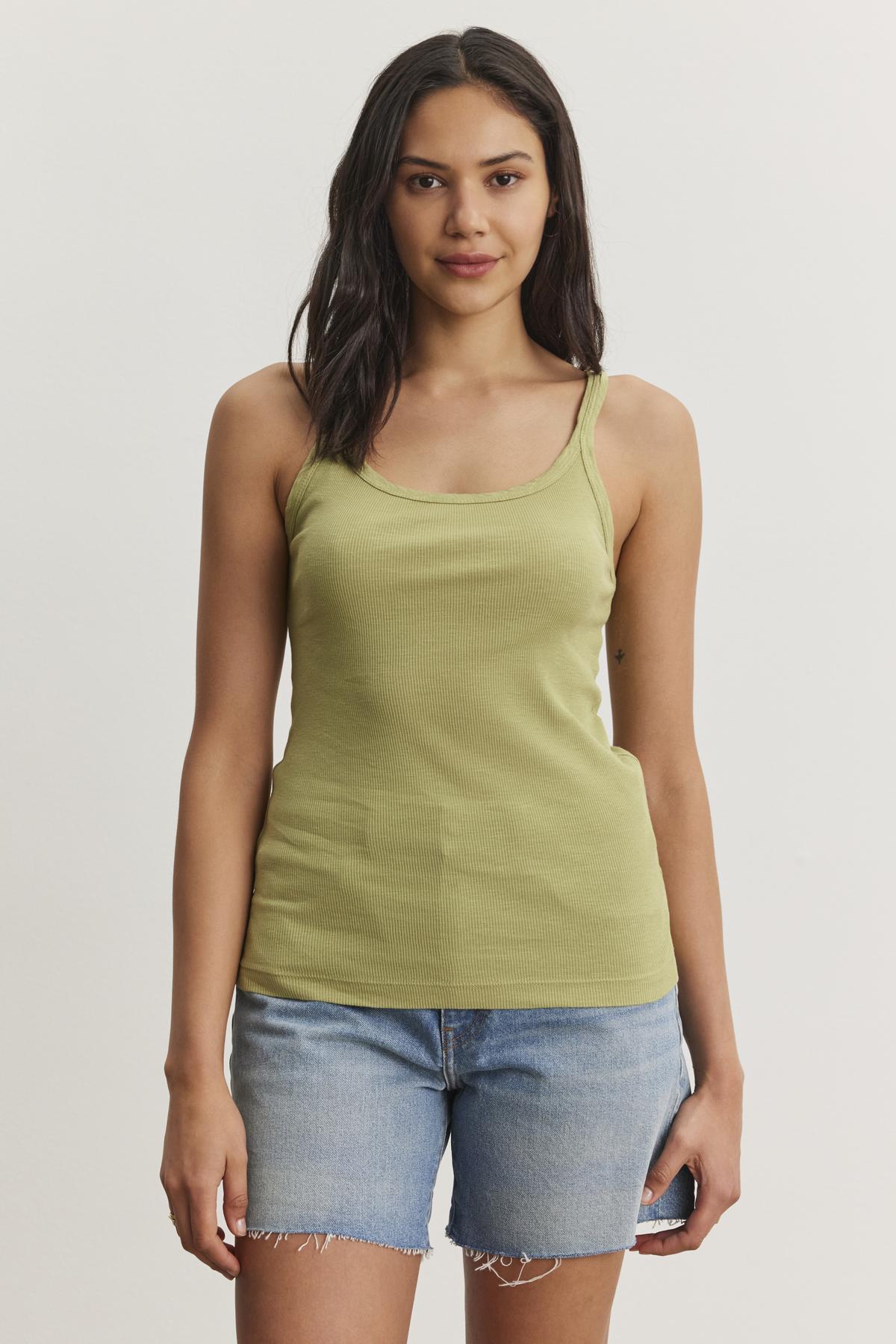 A person with long hair wearing a green ALIZA RIBBED COTTON LAYERING TANK by Velvet by Graham & Spencer and denim shorts is standing against a plain white background.-37104335683777