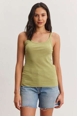 A person with long hair wearing a green ALIZA RIBBED COTTON LAYERING TANK by Velvet by Graham & Spencer and denim shorts is standing against a plain white background.