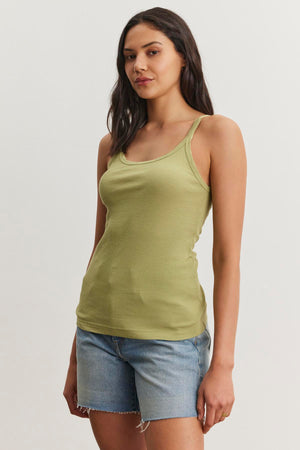 A woman wearing a green ALIZA RIBBED COTTON LAYERING TANK by Velvet by Graham & Spencer and denim shorts stands against a white background.