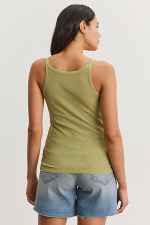 A person with long hair wearing a green ALIZA RIBBED COTTON LAYERING TANK by Velvet by Graham & Spencer and denim shorts is standing with their back to the camera.