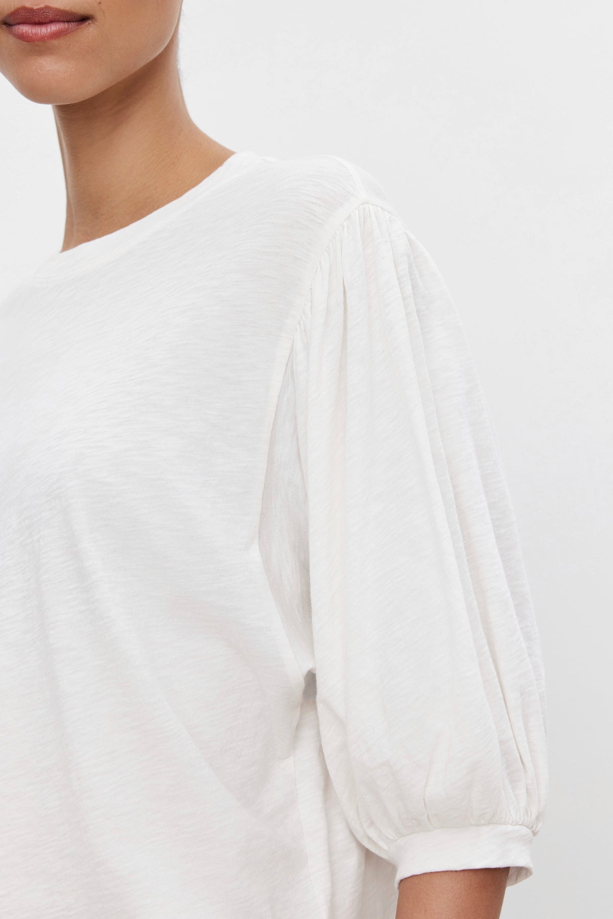   A person wearing the AMARA TEE by Velvet by Graham & Spencer, a loose-fitting white shirt with extra volume sleeves and banded cuffs, shown from the neck to the waist against a plain white background. 