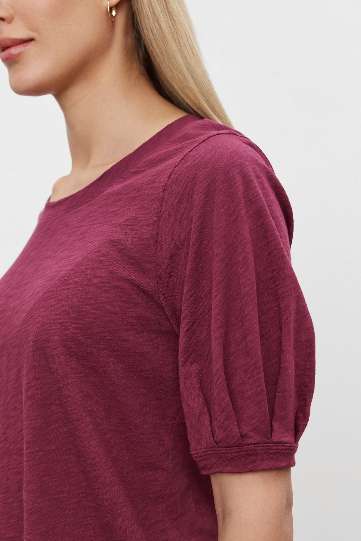   A person is wearing the ANABELLE TEE by Velvet by Graham & Spencer, a maroon scoop neck tee with puffed sleeves. The image focuses on the upper body and part of the left side of the face. 