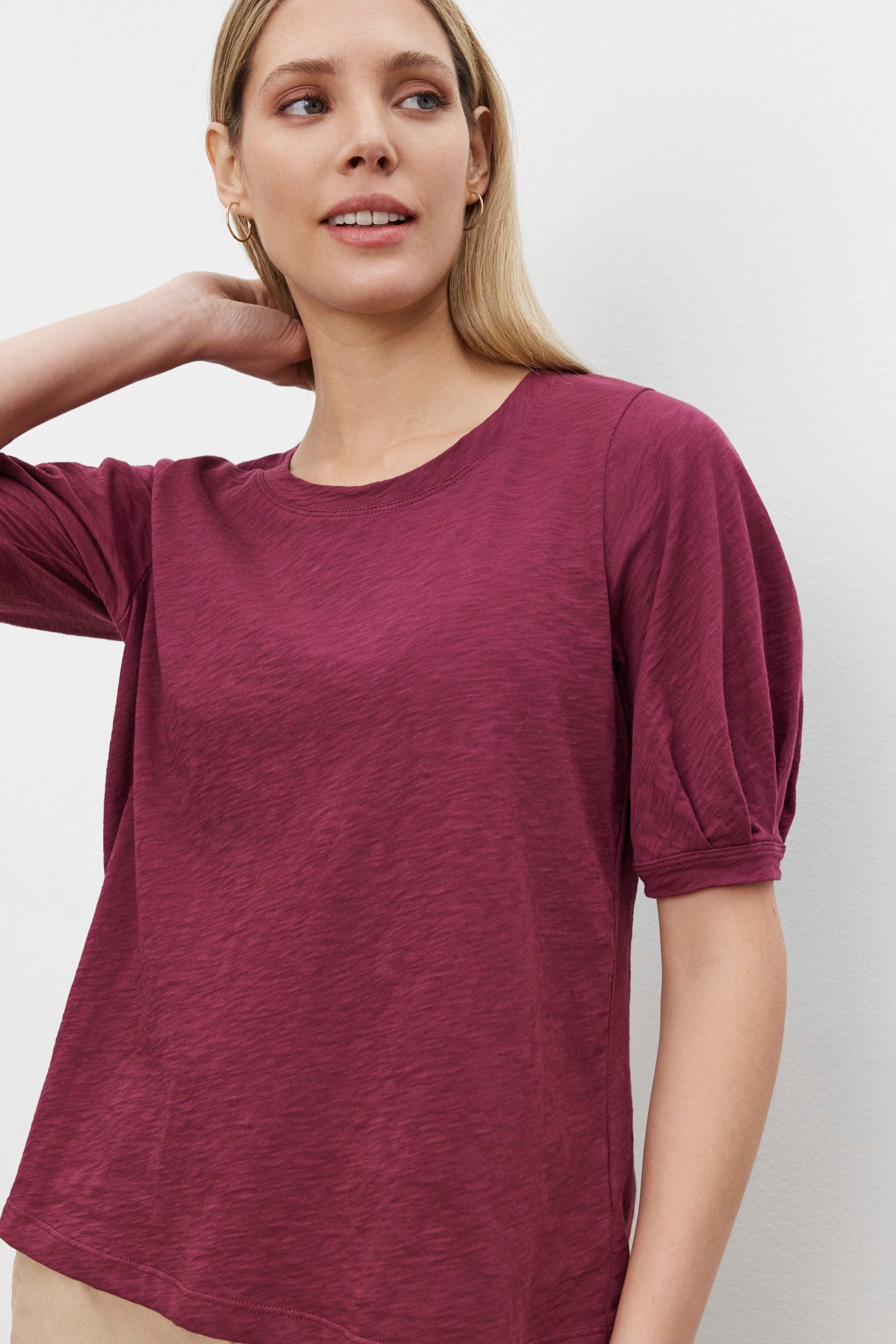   A person with long hair wearing the ANABELLE TEE by Velvet by Graham & Spencer, a maroon slub knit scoop neck tee, looks to one side while touching their hair. 