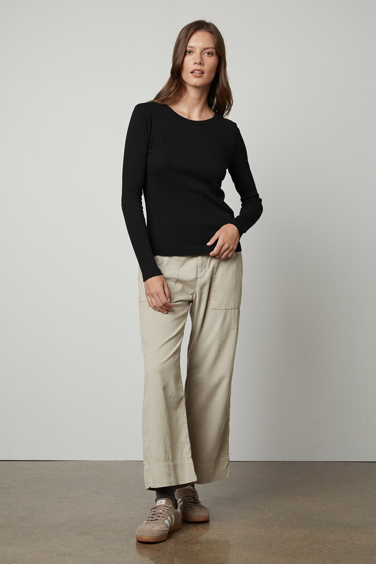 The model is wearing a black long-sleeved Velvet by Graham & Spencer BAYLER RIBBED SCOOP NECK TEE and beige wide leg pants.-35206768558273