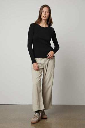 The model is wearing a black long-sleeved Velvet by Graham & Spencer BAYLER RIBBED SCOOP NECK TEE and beige wide leg pants.