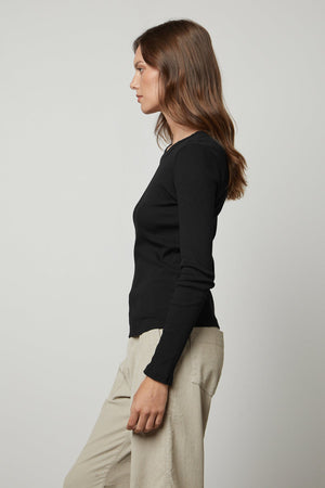 The model is wearing a Velvet by Graham & Spencer BAYLER RIBBED SCOOP NECK TEE top and beige trousers.