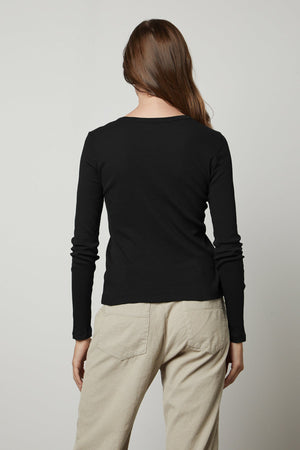 The back view of a woman wearing a Velvet by Graham & Spencer BAYLER RIBBED SCOOP NECK TEE and beige pants.