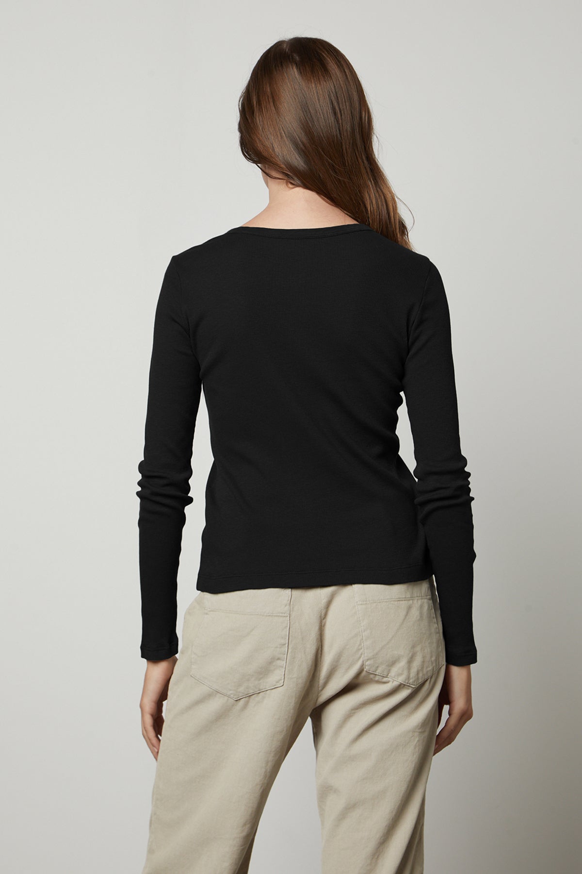   The back view of a woman wearing a Velvet by Graham & Spencer BAYLER RIBBED SCOOP NECK TEE and beige pants. 