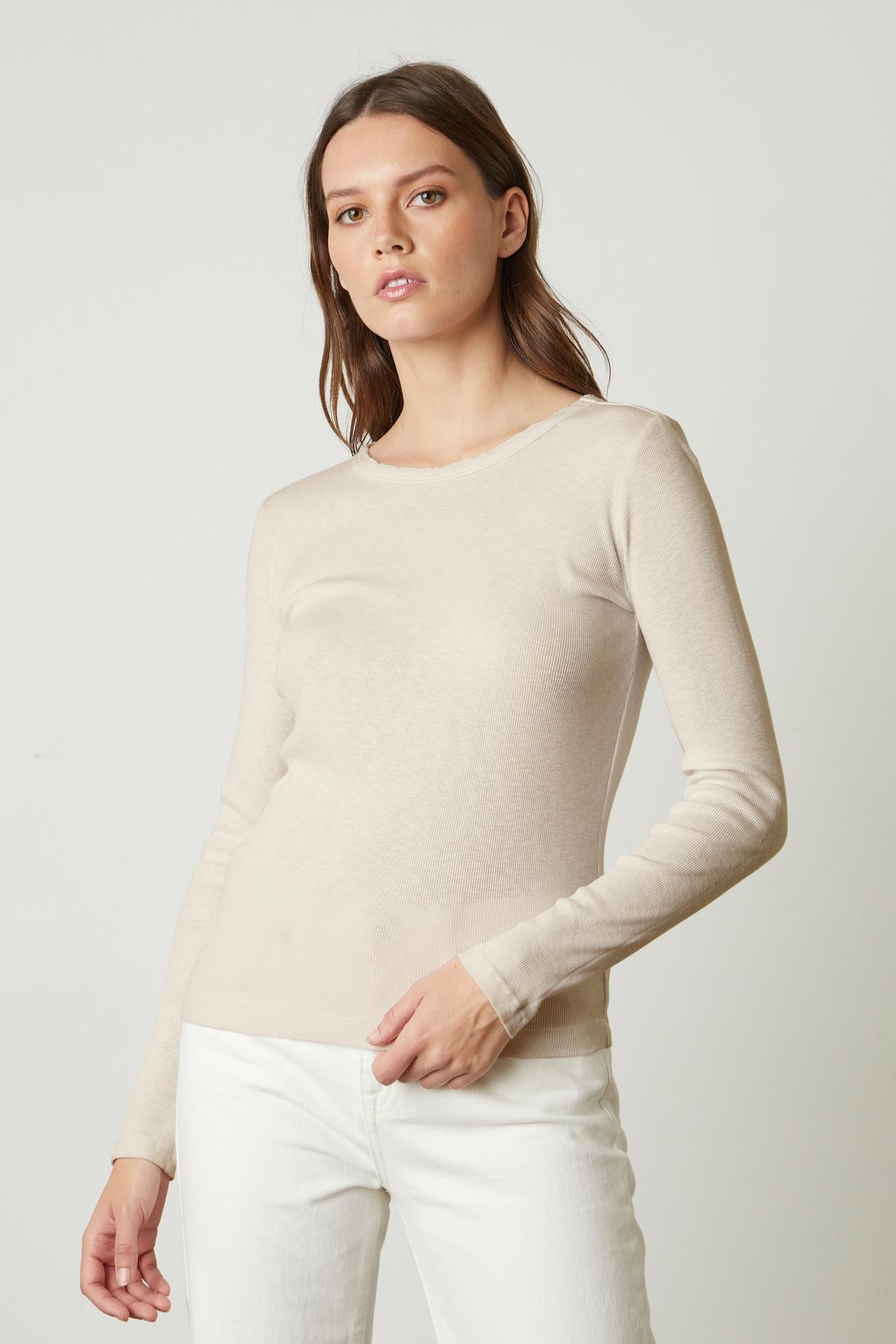   The model is wearing a rib-knit beige sweater and white jeans, perfect for layering over a Velvet by Graham & Spencer BAYLER RIBBED SCOOP NECK TEE. 
