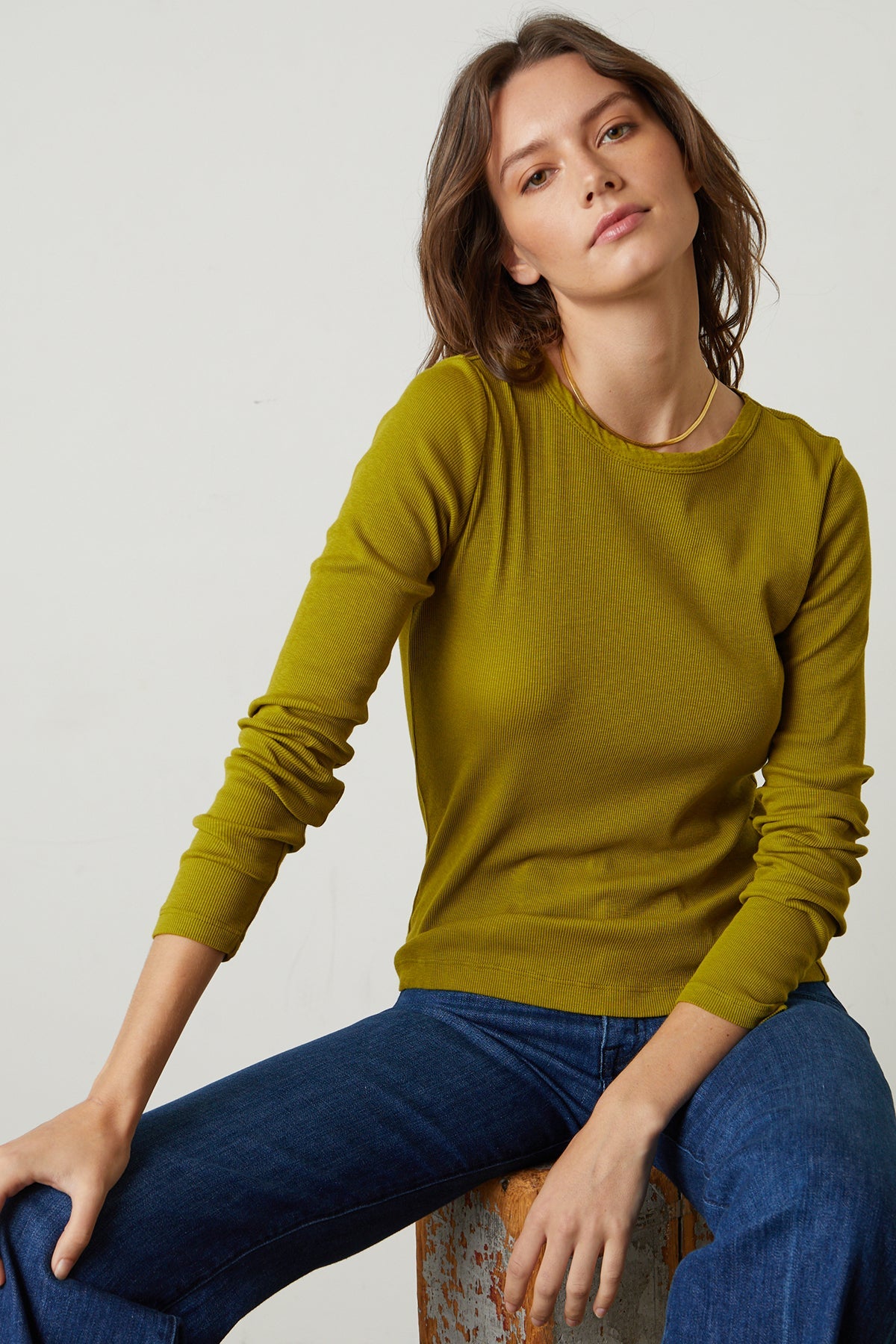 A woman is sitting on a stool in a Velvet by Graham & Spencer BAYLER RIBBED SCOOP NECK TEE.-26629804556481