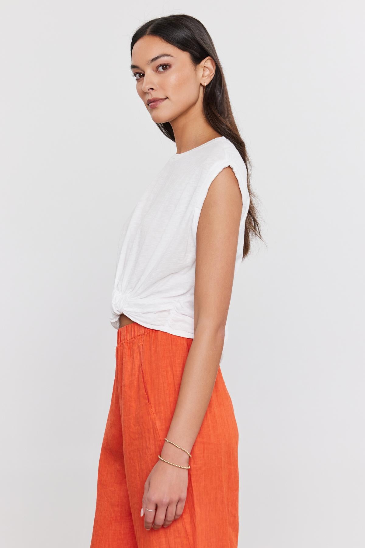   A woman in a white cotton Velvet by Graham & Spencer Callista tee with a crew neckline and orange pants, looking over her shoulder with a serene expression. 