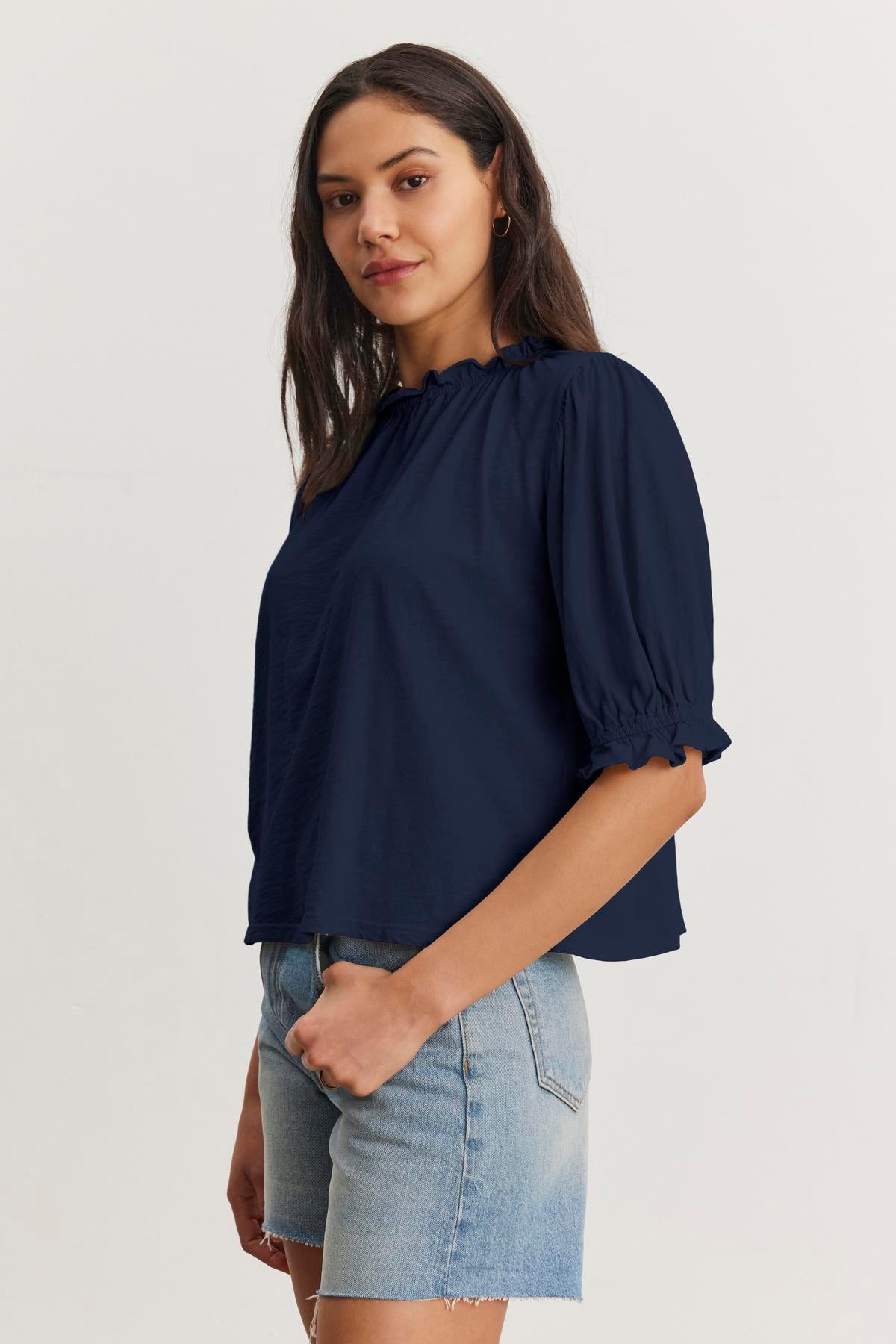   A woman wearing a Velvet by Graham & Spencer CARLENE TEE and denim shorts stands against a plain background. 