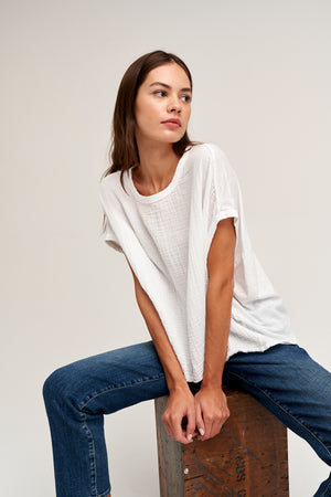 a woman wearing jeans and a Velvet by Graham & Spencer CORA BOXY TEE sitting on a wooden box.