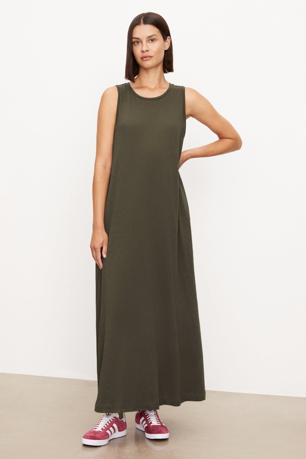   A woman wearing an olive green EDITH SLEEVELESS MAXI DRESS by Velvet by Graham & Spencer with a long silhouette and slash pockets. 