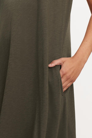 A woman wearing a green Velvet by Graham & Spencer Edith Sleeveless Maxi Dress with slash pockets.