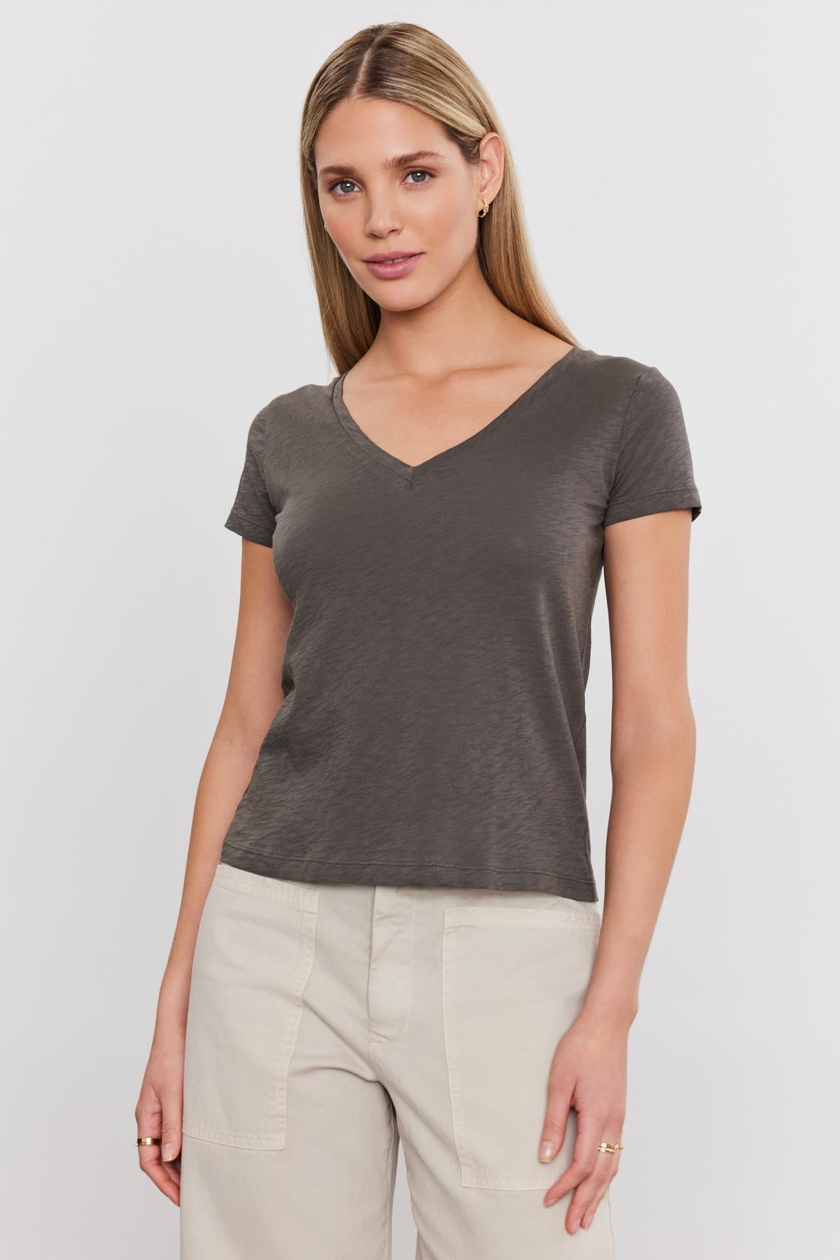 A woman in a Velvet by Graham & Spencer ELIAH TEE and beige pants standing against a white background.-36910213497025