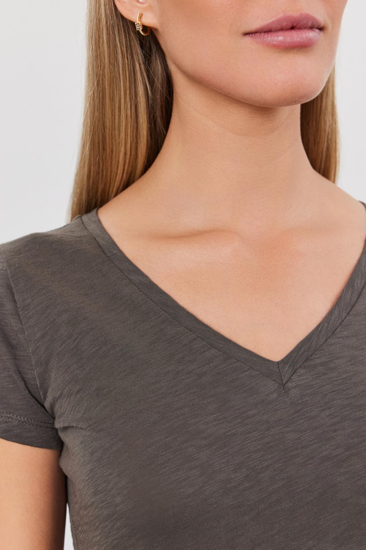   Close-up of a woman wearing a gray cotton slub Eliah tee by Velvet by Graham & Spencer, focusing on the v-neckline and upper chest area, with her face partially visible. 