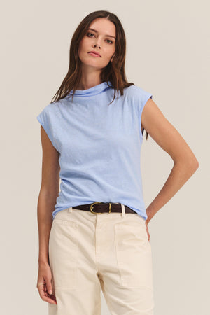 A woman wearing the FLETCHER TEE from Velvet by Graham & Spencer, paired with cream-colored pants and a black belt, stands against a plain background.