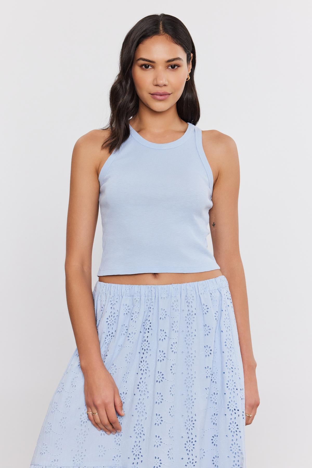 Woman wearing a light blue Velvet by Graham & Spencer HARLA RIBBED CROPPED TANK TOP and matching eyelet skirt, standing against a plain white background.-36752885940417