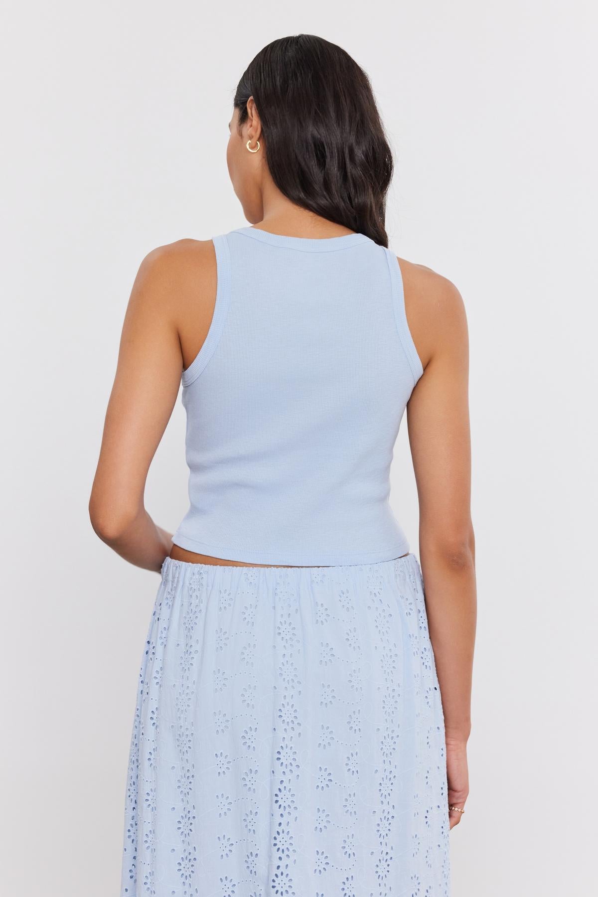   Woman standing with her back to the camera, wearing a light blue Velvet by Graham & Spencer HARLA RIBBED CROPPED TANK TOP and a blue eyelet skirt. 