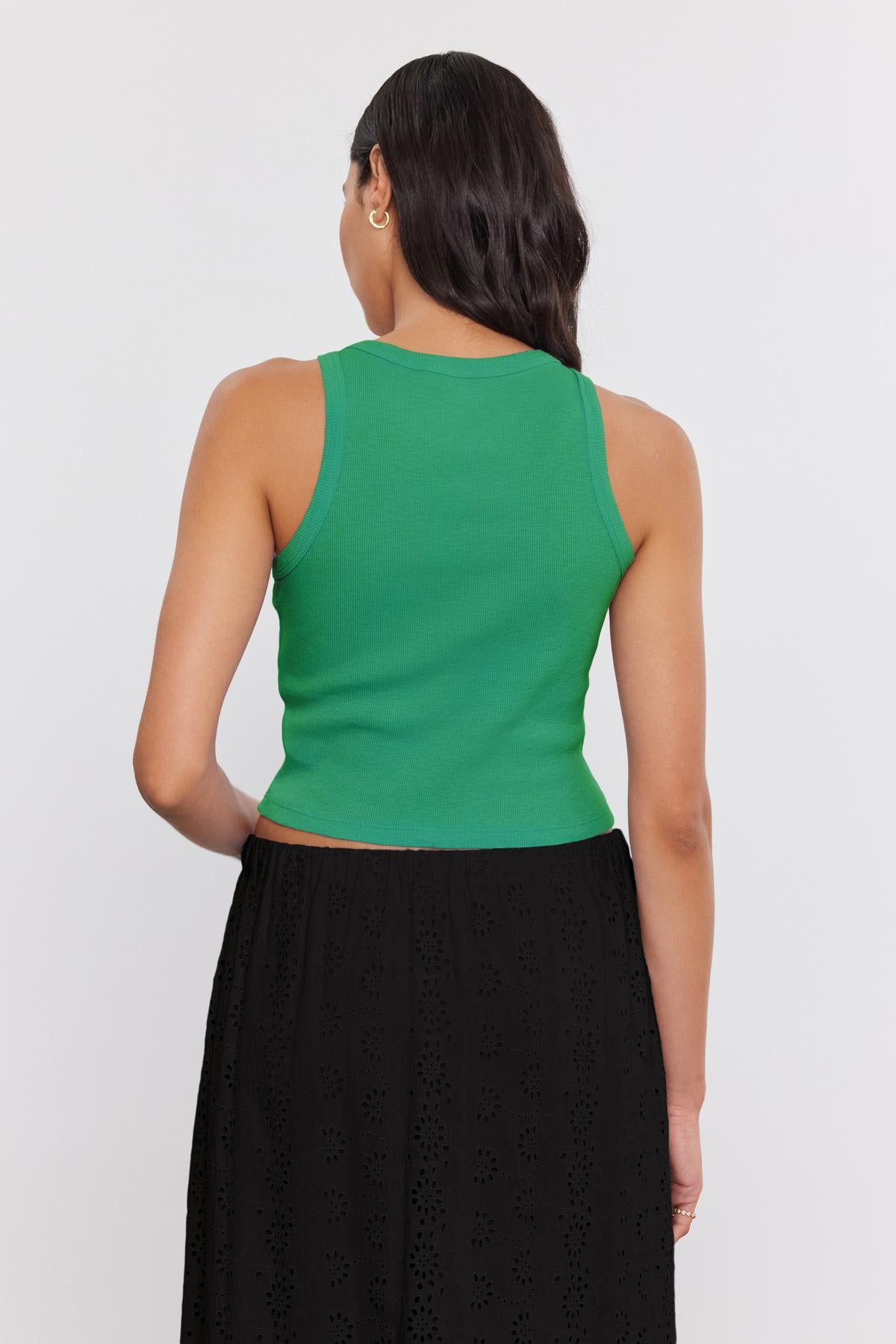   A person with long dark hair stands facing away, wearing a HARLA RIBBED CROPPED TANK TOP from Velvet by Graham & Spencer and a black skirt. 