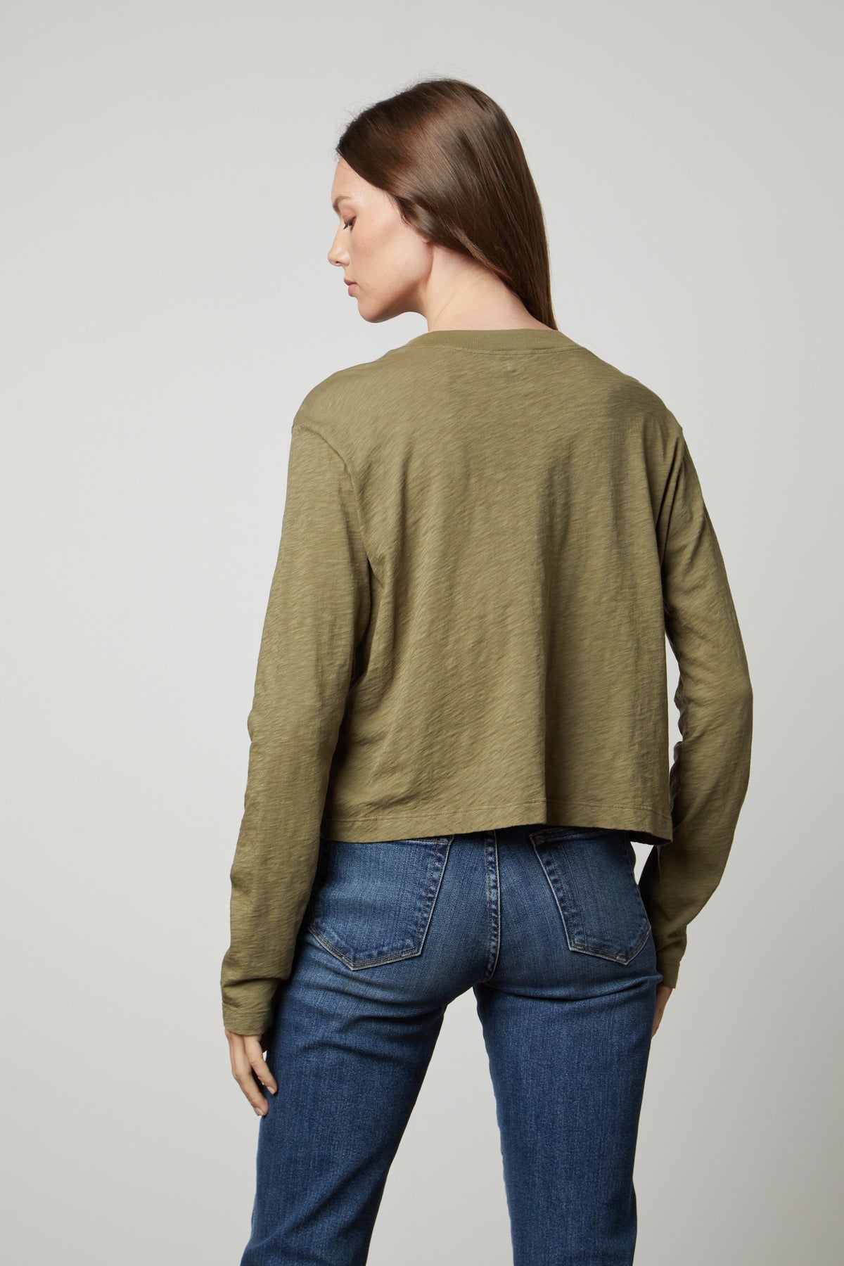The view of a woman wearing the Velvet by Graham & Spencer HEATHER CREW NECK CROPPED TEE in olive green jeans and a long-sleeved shirt.-35655736131777