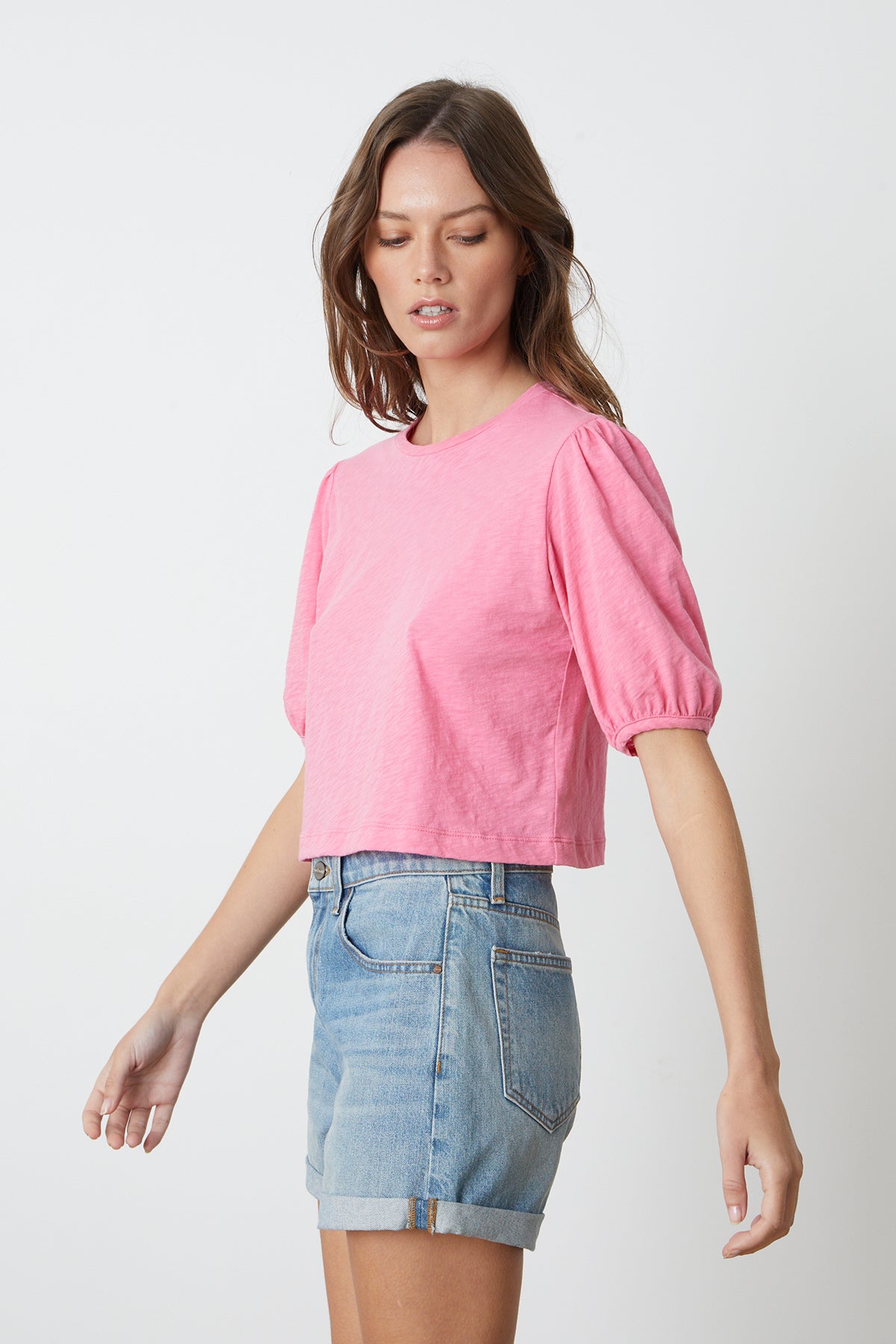 a model wearing a pink HILARY PUFF SLEEVE CROPPED TEE by Velvet by Graham & Spencer and denim shorts.-26342696714433