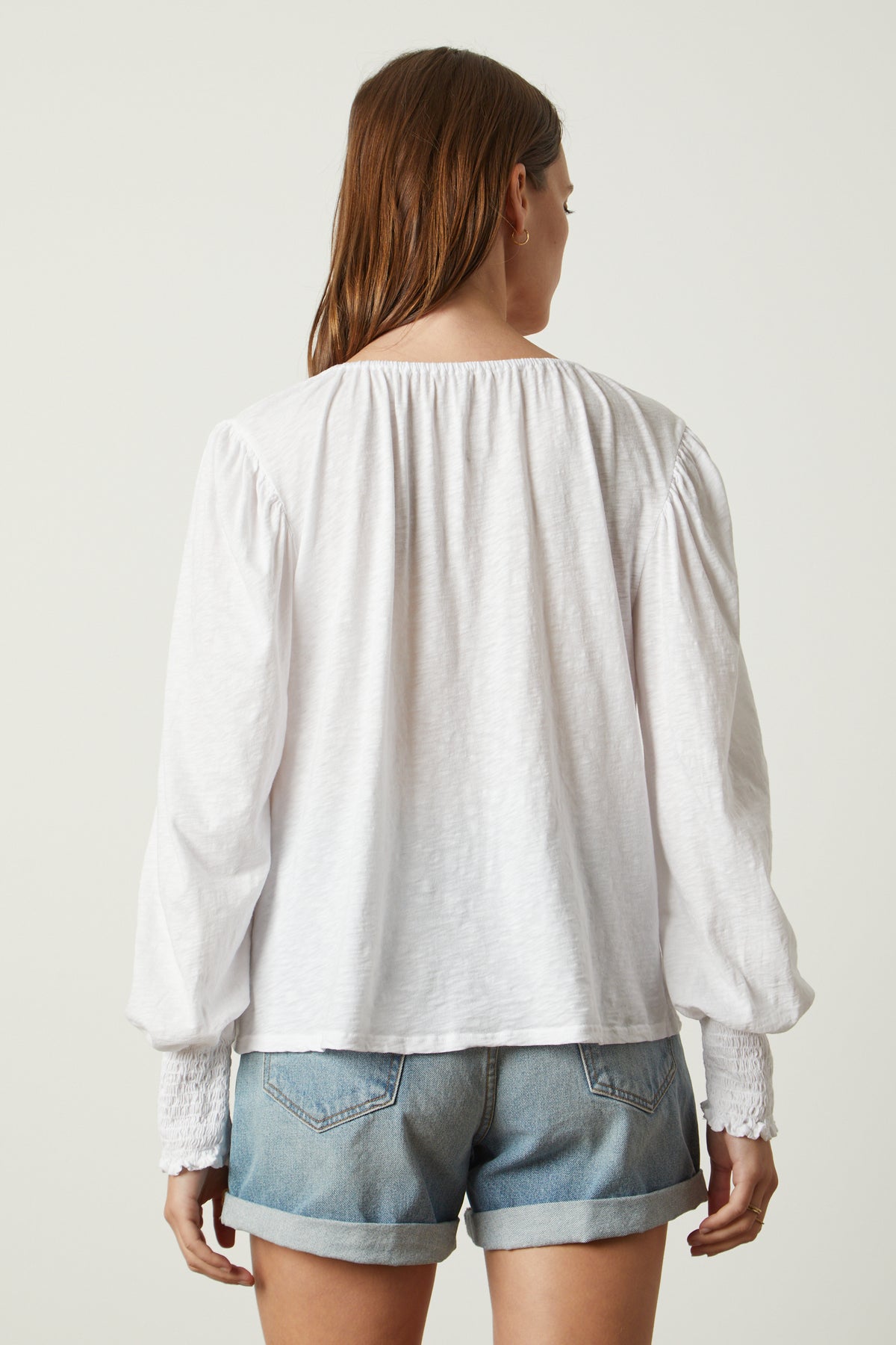 the back view of a woman wearing IRINA SPLIT NECK TEE by Velvet by Graham & Spencer denim shorts and a white blouse.-26317135413441