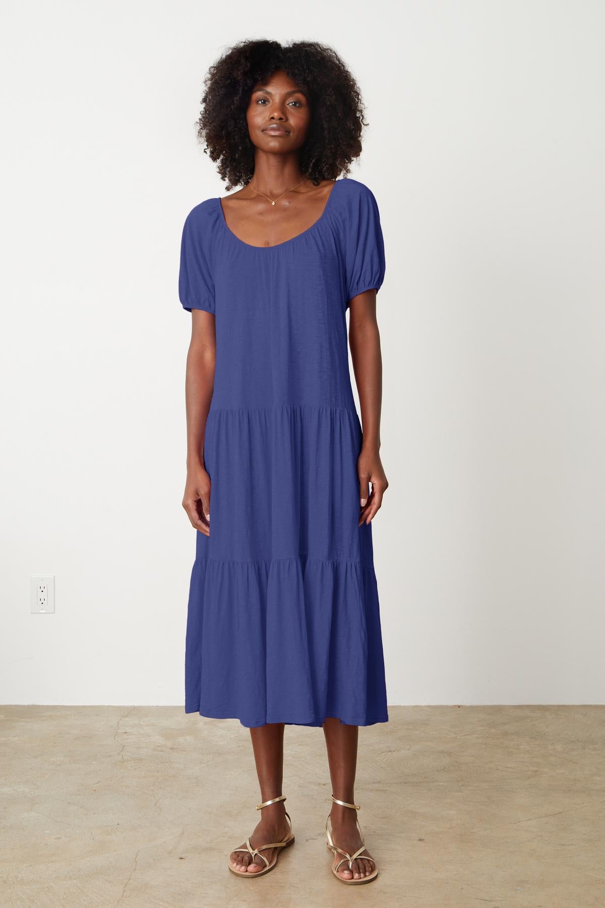   A woman wearing a blue JANE SCOOP NECK TIERED DRESS by Velvet by Graham & Spencer and sandals. 