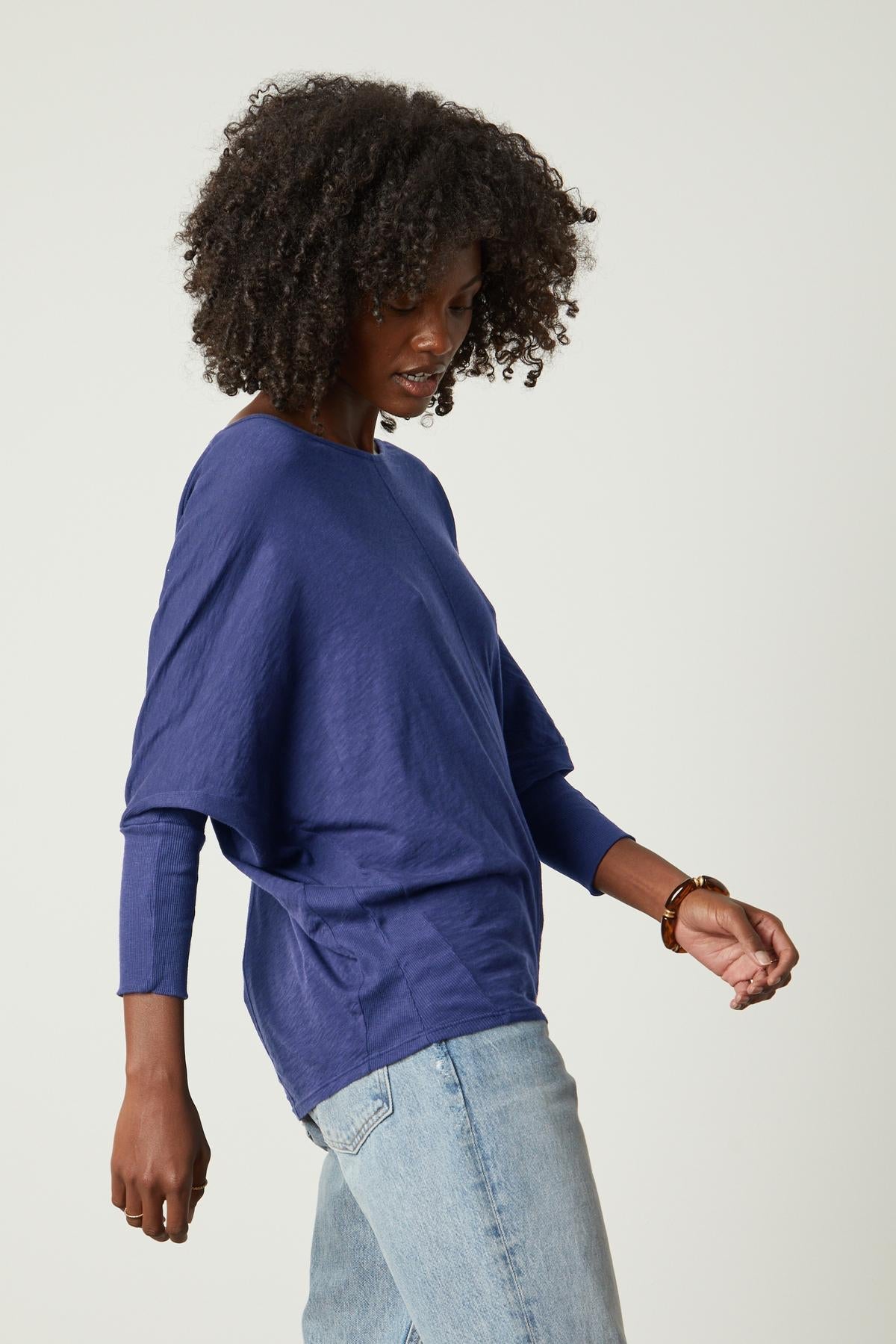   A woman wearing jeans and a blue Velvet by Graham & Spencer JOSS DOLMAN SLEEVE TEE top. 