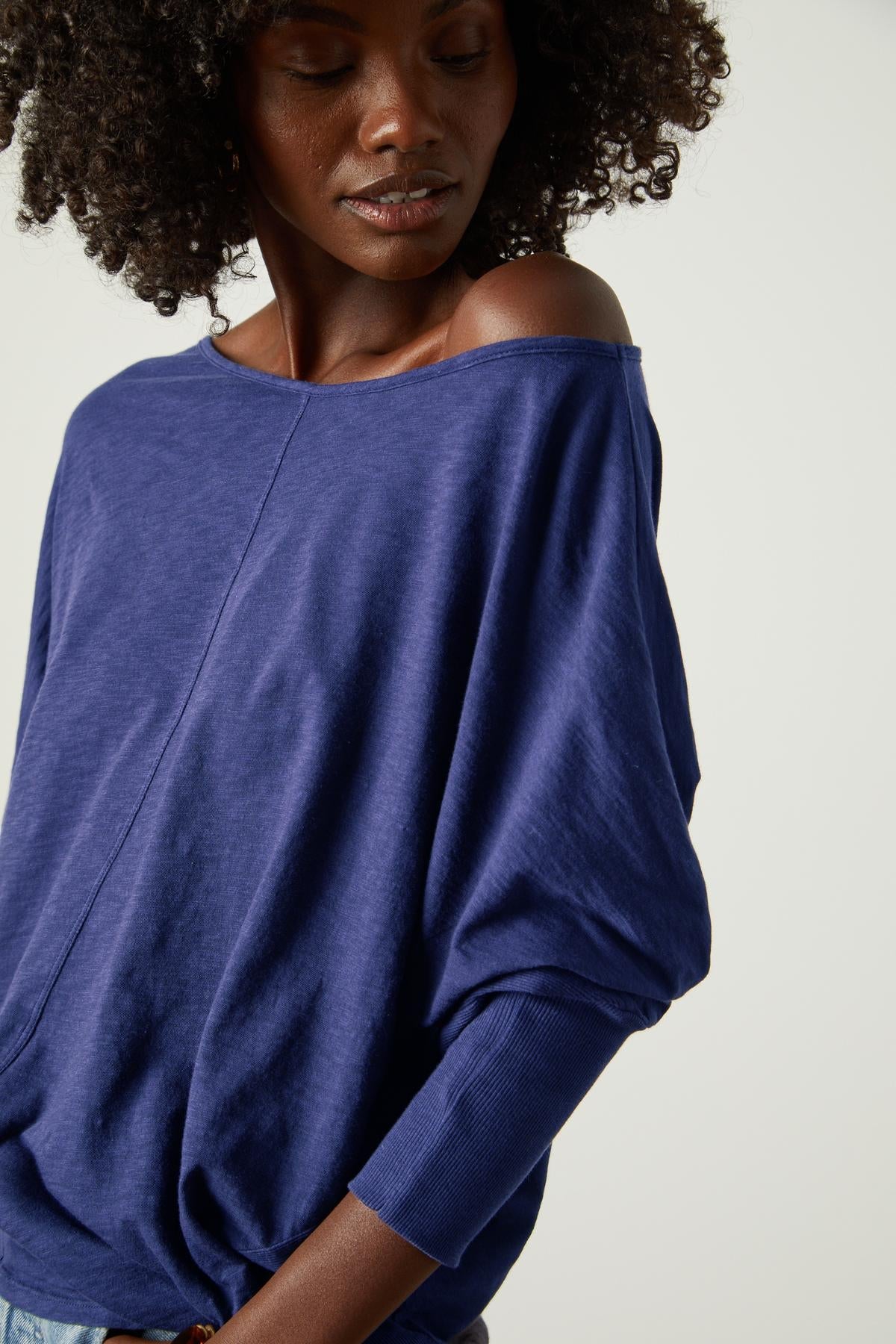 A woman wearing a blue JOSS DOLMAN SLEEVE TEE by Velvet by Graham & Spencer top with ruffled sleeves.-35206719275201