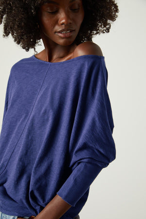 A woman wearing a blue JOSS DOLMAN SLEEVE TEE by Velvet by Graham & Spencer top with ruffled sleeves.