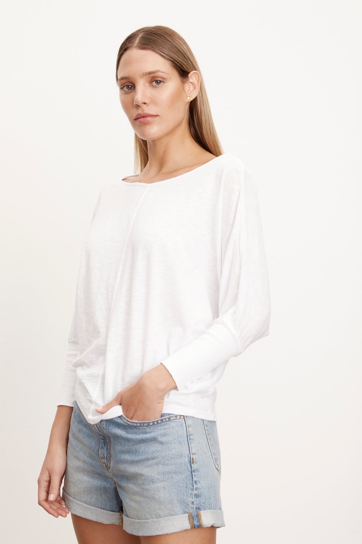   Woman wearing Joss Tee in white with dolman sleeve and denim shorts, hand in front shorts pocket, 3/4 view 