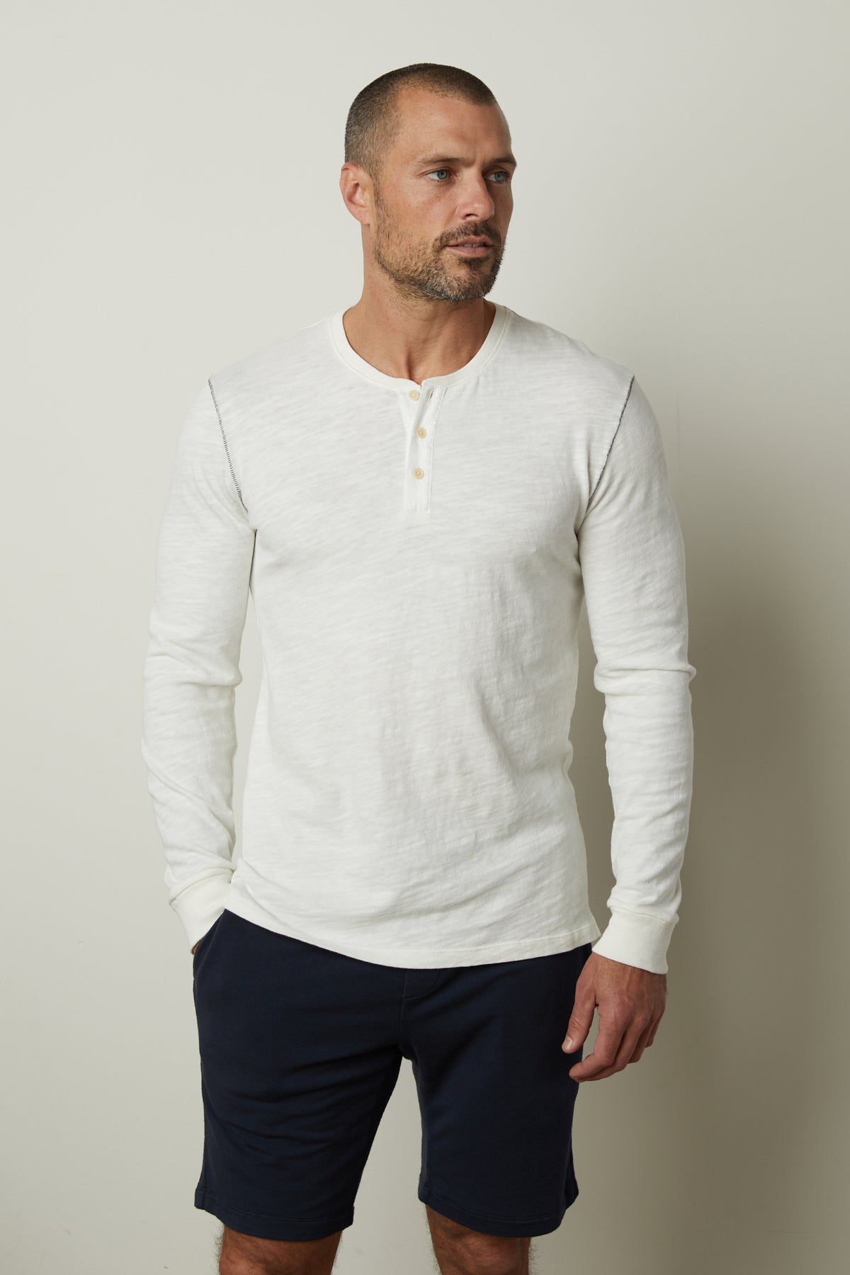 A man wearing a white Gabe Henley shirt by Velvet by Graham & Spencer in a cotton slub fabric, paired with blue shorts.-35662699397313