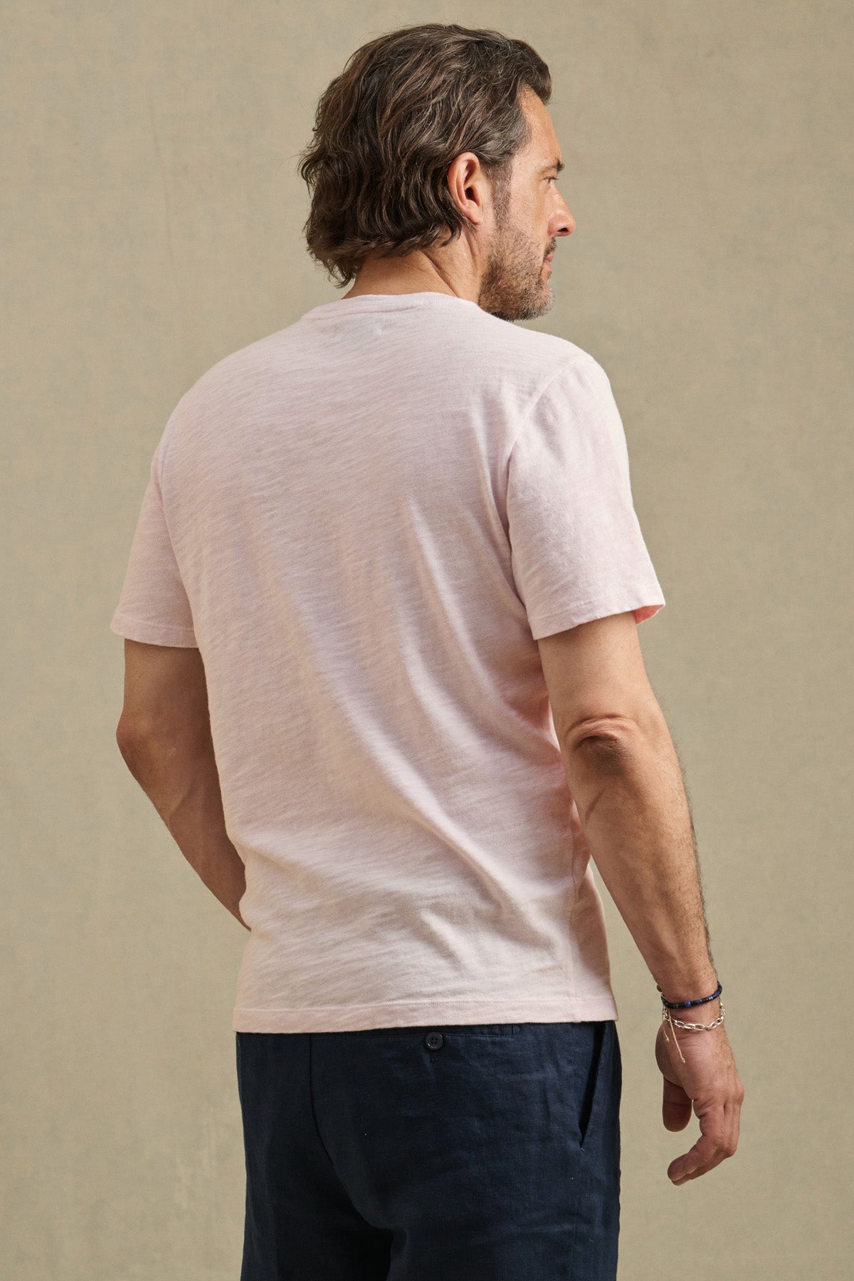 A man with short brown hair wears the Velvet by Graham & Spencer PAUL TEE in light pink and dark pants, standing with his back to the camera against a plain background.-41491030835393