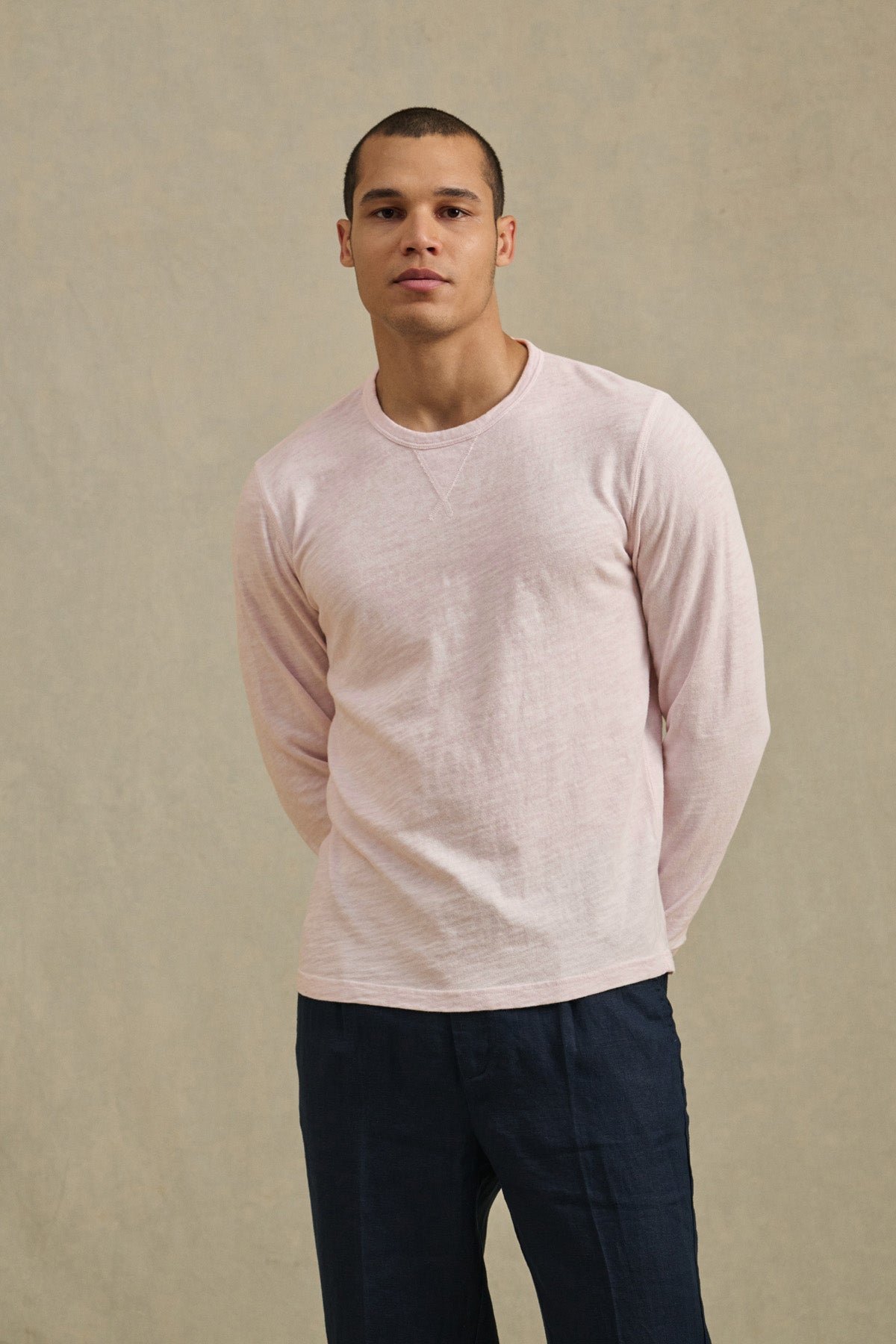 Wearing the ZANE TEE by Velvet by Graham & Spencer in light pink with long sleeves, and dark pants, a person stands against a plain beige background facing forward, hands behind their back.-41480104280257