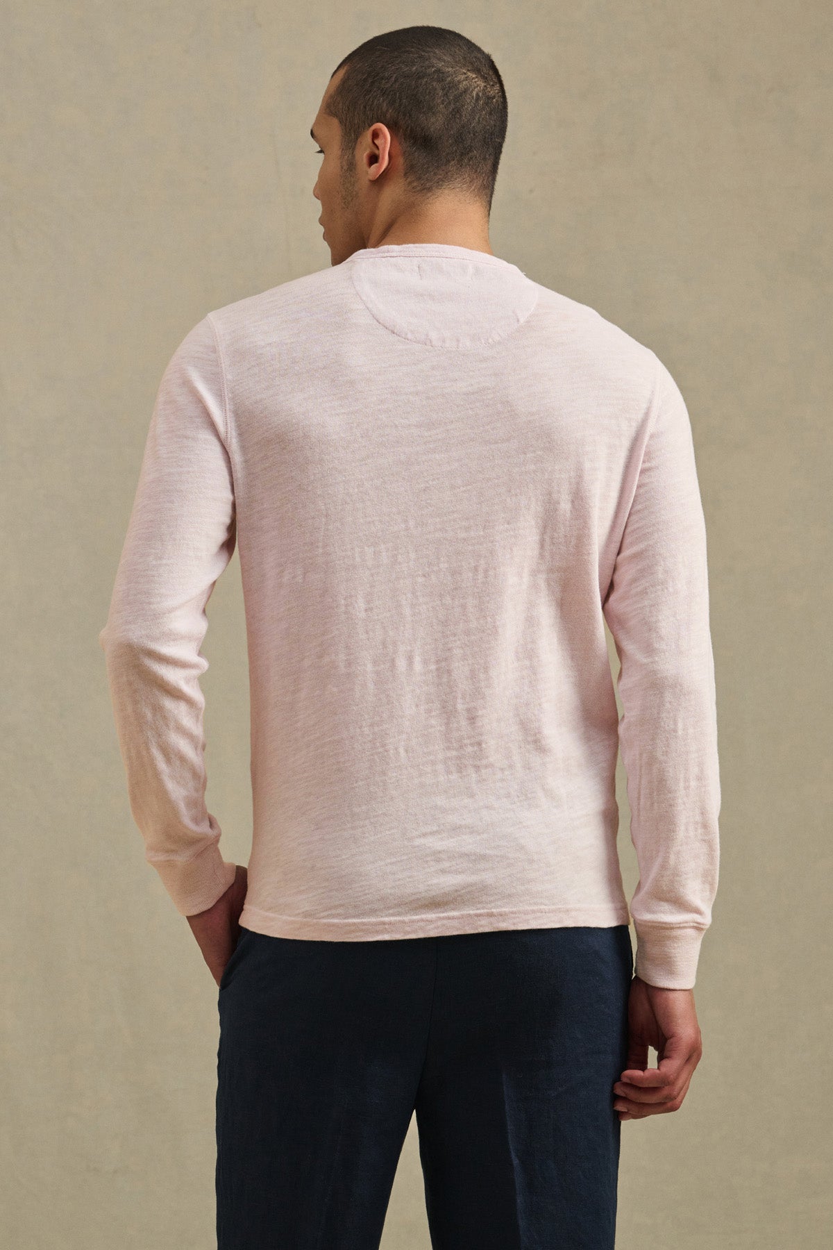 A person faces away from the camera, wearing the ZANE TEE by Velvet by Graham & Spencer in light pink cotton slub with dark pants, set against a plain beige background.