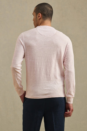 A person faces away from the camera, wearing the ZANE TEE by Velvet by Graham & Spencer in light pink cotton slub with dark pants, set against a plain beige background.