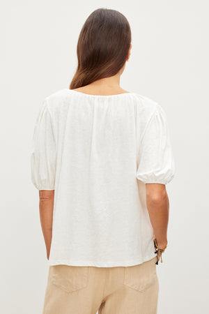 The back view of a woman wearing a white LEE RELAXED TEE by Velvet by Graham & Spencer and tan pants.