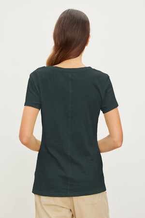 A person with long hair is shown from the back, wearing a dark green short-sleeved V-neck LILITH TEE by Velvet by Graham & Spencer and beige pants, standing against a plain white background. The shirt's cotton slub fabric adds a touch of luxurious softness.