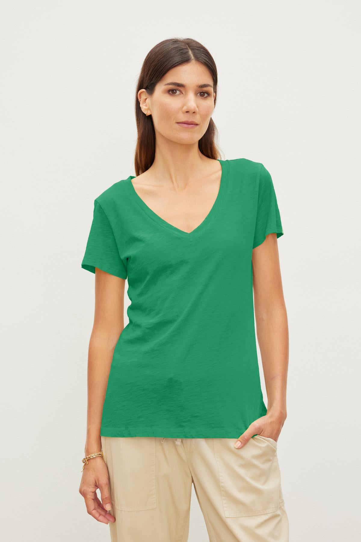 A woman in a Velvet by Graham & Spencer LILITH COTTON SLUB V-NECK TEE and beige pants, standing against a plain white background, looking at the camera.-36910215037121