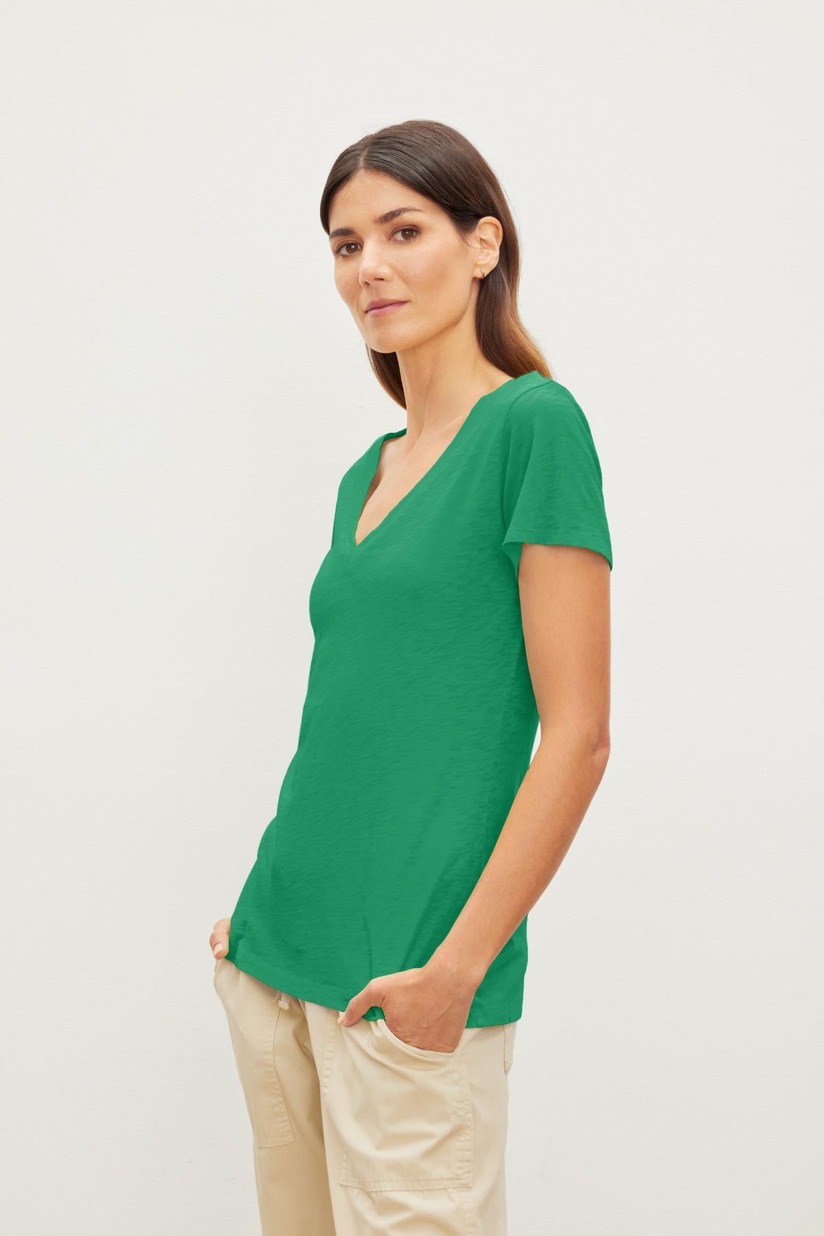   Woman in a LILITH COTTON SLUB V-NECK TEE by Velvet by Graham & Spencer and beige pants standing against a white background, looking at the camera with a soft smile. 