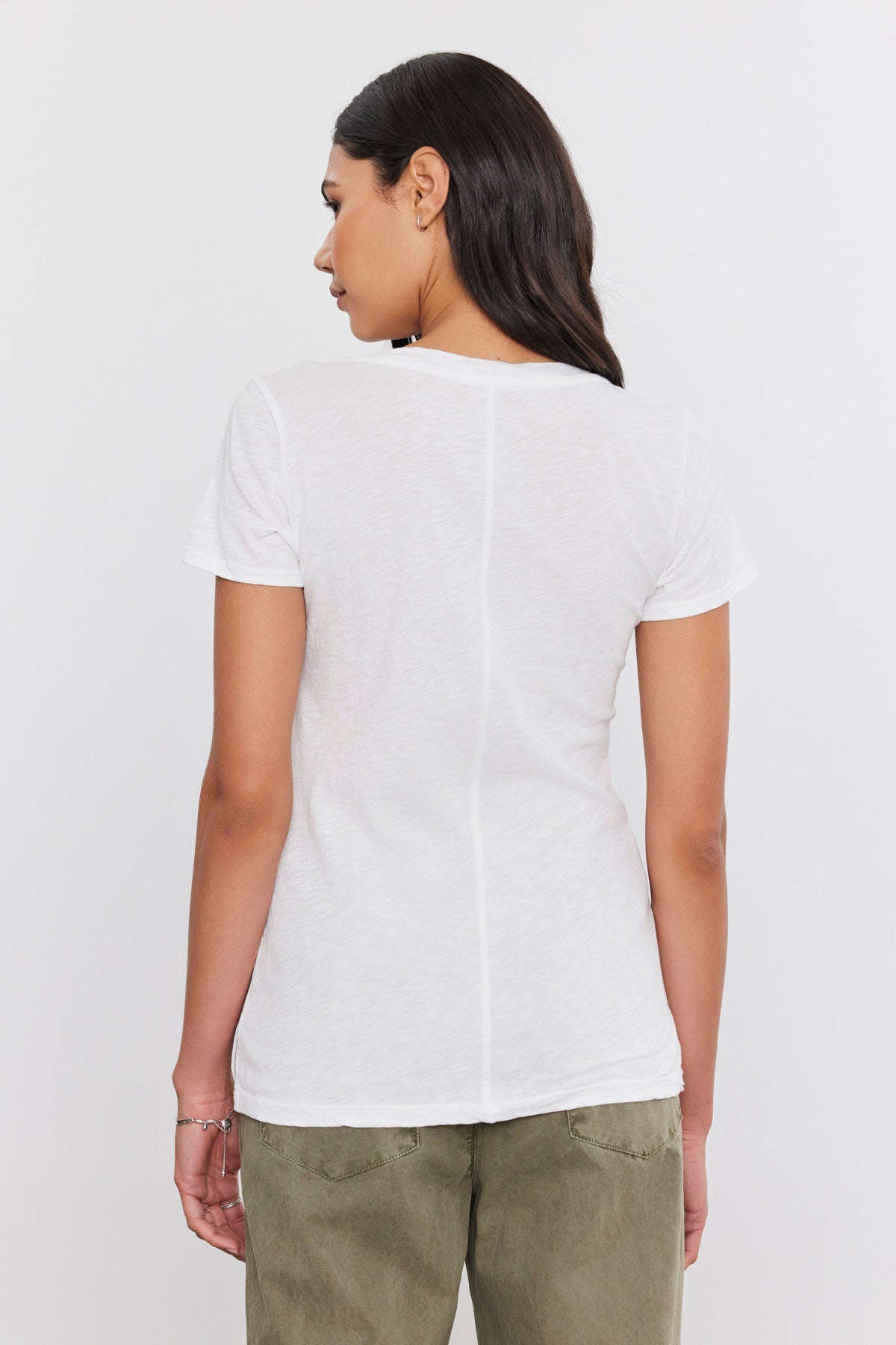 The back view of a woman wearing a LILITH COTTON SLUB V-NECK TEE by Velvet by Graham & Spencer made of luxe cotton slub and green pants showcases her preppy style.-35586083487937
