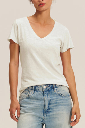 A person wearing the LILITH TEE by Velvet by Graham & Spencer, a white cotton slub V-neck, and light blue jeans stands against a neutral background.