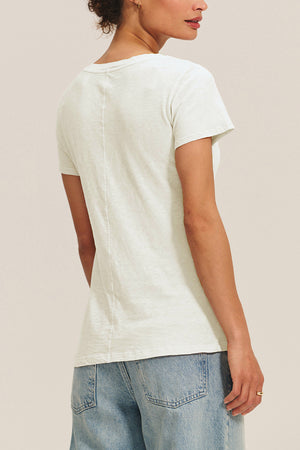 A woman shown from the back wears the Velvet by Graham & Spencer LILITH TEE, a plain white cotton slub V-neck, paired with light blue denim jeans against a neutral background.